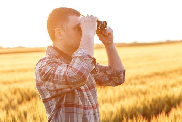 Mann steht auf dem Feld und schaut mit dem Feldstecher in Richtung des rechten Bildrandes