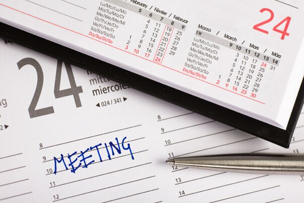 Ein Planer mit dem Eintrag Meeting. Ein Kugelschreiber liegt daneben