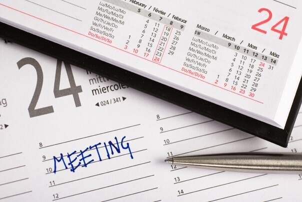 Ein Planer mit dem Eintrag Meeting. Ein Kugelschreiber liegt daneben