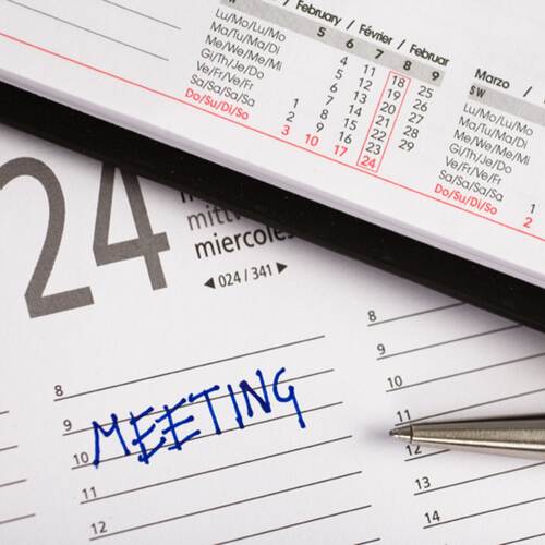 Ein Planer mit dem Eintrag Meeting. Ein Kugelschreiber liegt daneben
